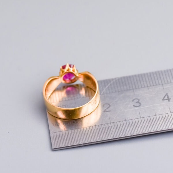 Elegant gold ring with pink gemstone, displayed against a white background with a measuring scale for size reference.